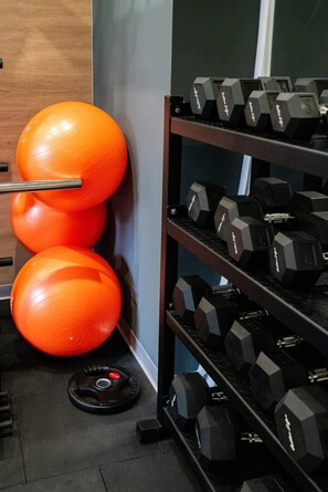 A gym with orange exercise balls and a rack of black dumbbells.
