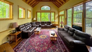 A spacious living room with a large sectional sofa, a patterned rug, and large windows offering a view of the outdoors.