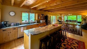 A spacious kitchen with wooden beams, a large island with stools, and a dining area with chairs.