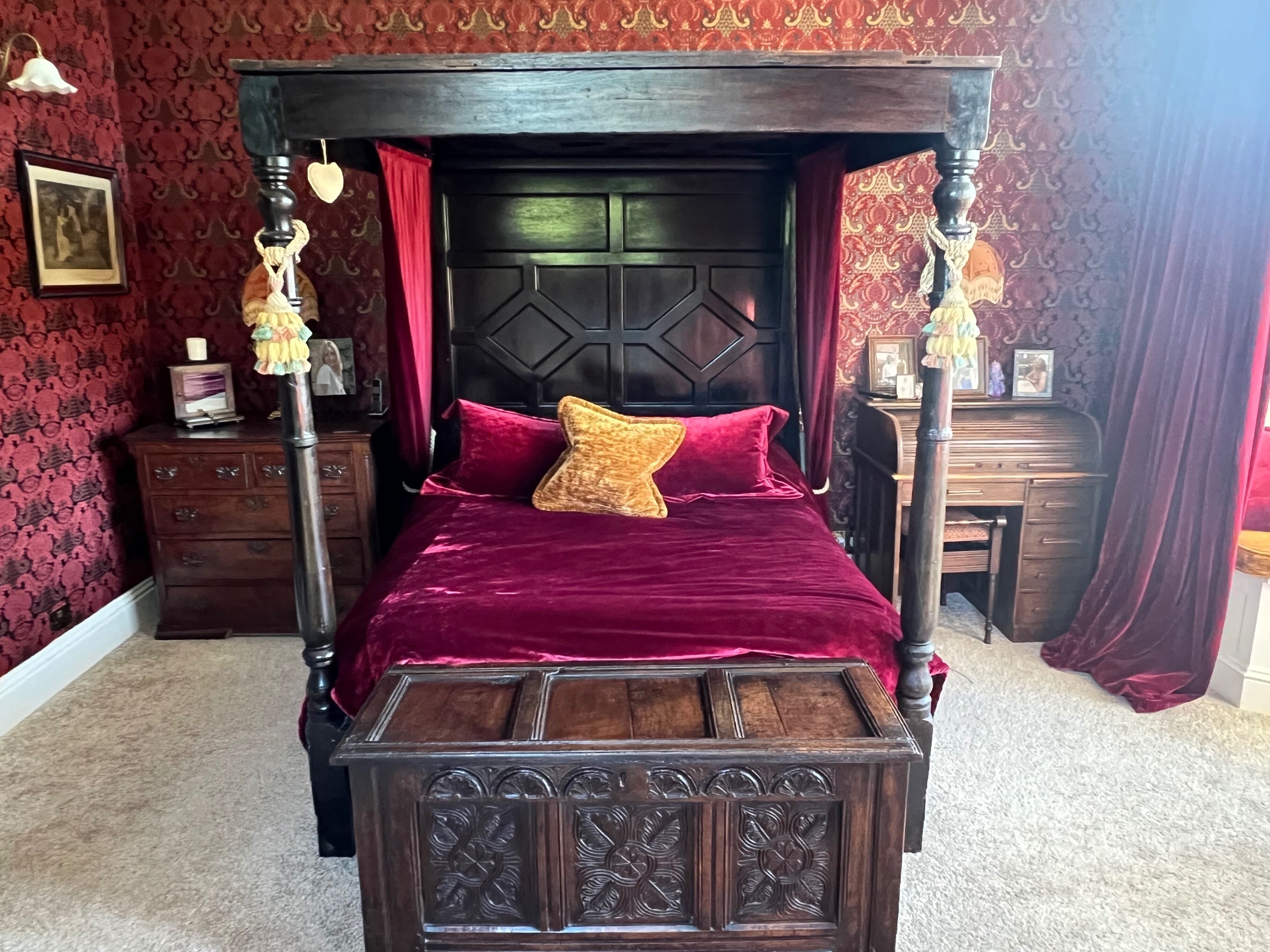 Una cama con dosel de madera oscura y ropa de cama de terciopelo rojo.