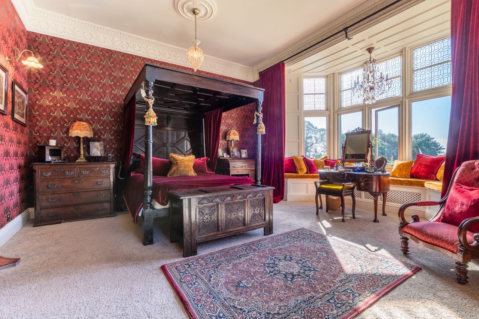 A traditional bedroom with a four-poster bed, a wooden dresser, a desk, and a chair.