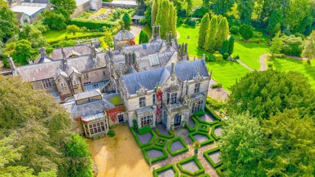 Vue aérienne d’un domaine historique, avec un grand bâtiment central entouré de jardins aménagés et de constructions plus petites.