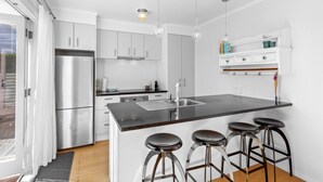 A modern kitchen with a central island, stainless steel appliances, and bar stools. - Cosy Retreat in Rothesay Bay| by Furnished Rentals (Auckland)
