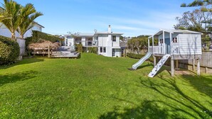 A two-story house with a backyard featuring a slide and a playhouse. - Cosy Retreat in Rothesay Bay| by Furnished Rentals (Auckland)