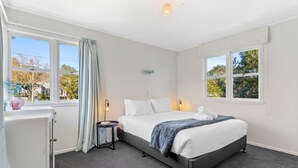 A bedroom with a bed, bedside tables, and windows. - Cosy Retreat in Rothesay Bay| by Furnished Rentals (Auckland)