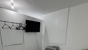 Quarto com cama, televisão fixada na parede, cabideiro e pequena mesa com toalhas.