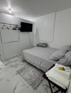 Ein Schlafzimmer mit einem Bett, einem an der Wand montierten Fernseher, einem Kleiderständer und einem kleinen Tisch mit Handtüchern.