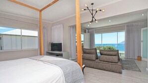 Une chambre à coucher avec un lit à baldaquin, une télévision et un canapé donnant sur la mer.