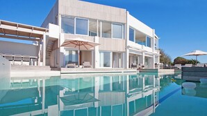 Une maison moderne à deux étages, dotée d’une piscine, d’un espace salon extérieur et de grandes fenêtres.