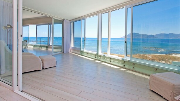 Une pièce spacieuse avec de grandes fenêtres donnant sur la mer, une porte-fenêtre coulissante qui mène à un espace extérieur et un parquet en bois de couleur claire.