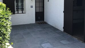 A building with a tiled patio, a black door, and a window with shutters. - Mazet en camargue in a secure, comfortable residence 8 minutes from les saintes (Saintes-Maries-de-la-Mer)