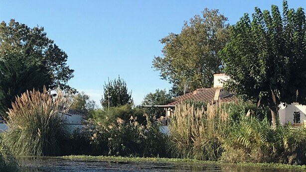 A serene pond with reflections, surrounded by lush greenery and a white building with a tiled roof. - Mazet en camargue in a secure, comfortable residence 8 minutes from les saintes (Saintes-Maries-de-la-Mer)