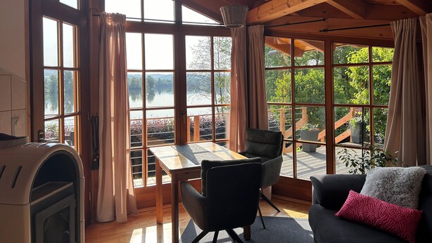 A cozy room with large windows, a wooden ceiling, a table, chairs, and a couch. - *Lake House* – an idyllic vacation home right on the lake with a terrace and a fireplace (Lauenförde)