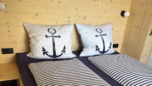 A bed with striped bedding, two pillows with anchor designs, and a wooden headboard. - *Lake House* – an idyllic vacation home right on the lake with a terrace and a fireplace (Lauenförde)