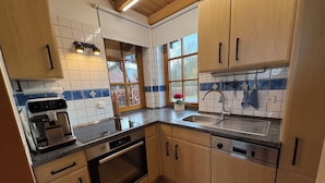 A kitchen with wooden cabinets, a built-in oven, a coffee machine, a sink, and a window with a view of trees. - *Lake House* – an idyllic vacation home right on the lake with a terrace and a fireplace (Lauenförde)