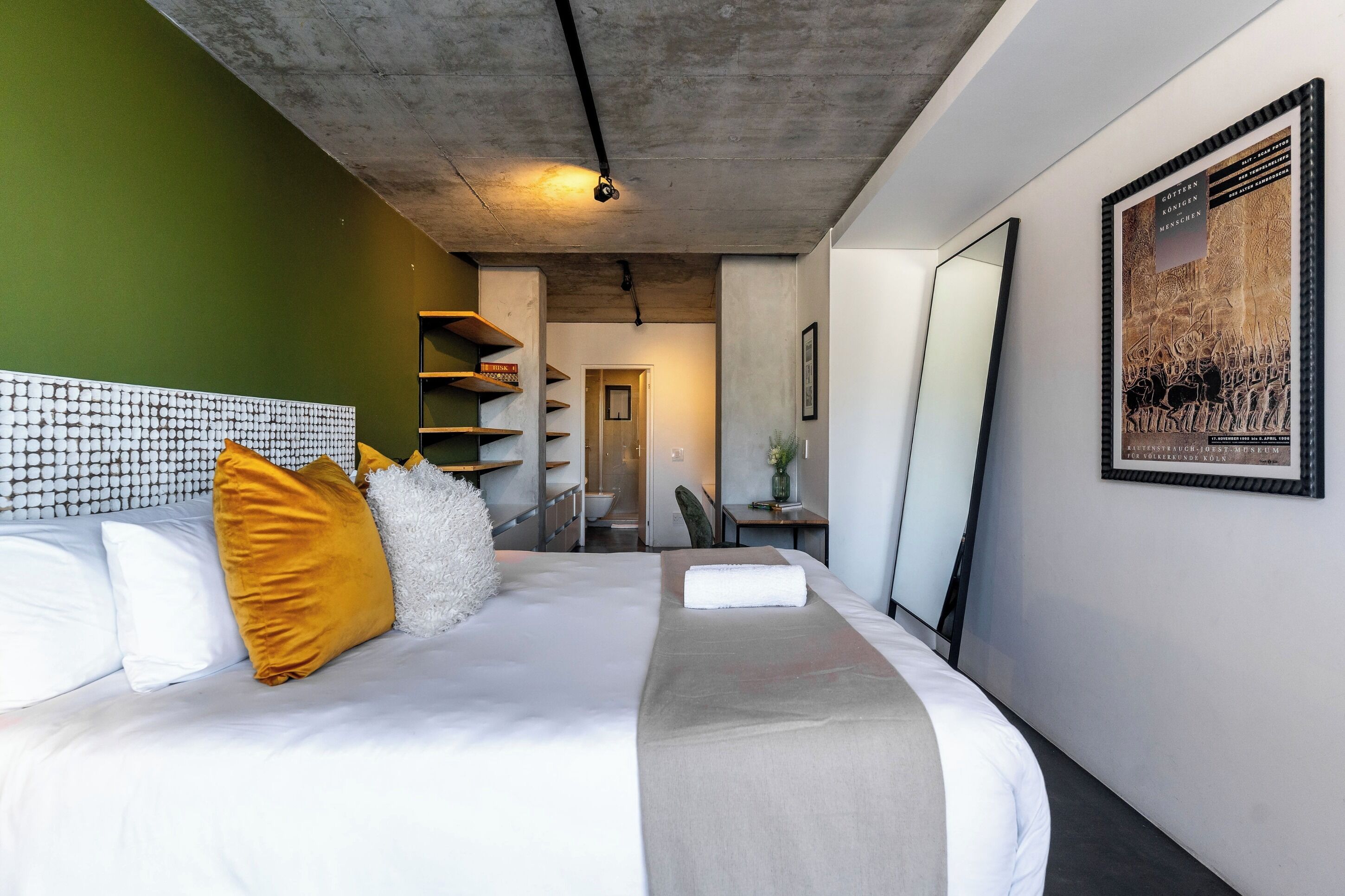 Ein modernes Hotelzimmer mit einem großen Bett, einem Kopfteil mit geometrischem Muster, einem Spiegel und einem gerahmten Bild an der Wand.