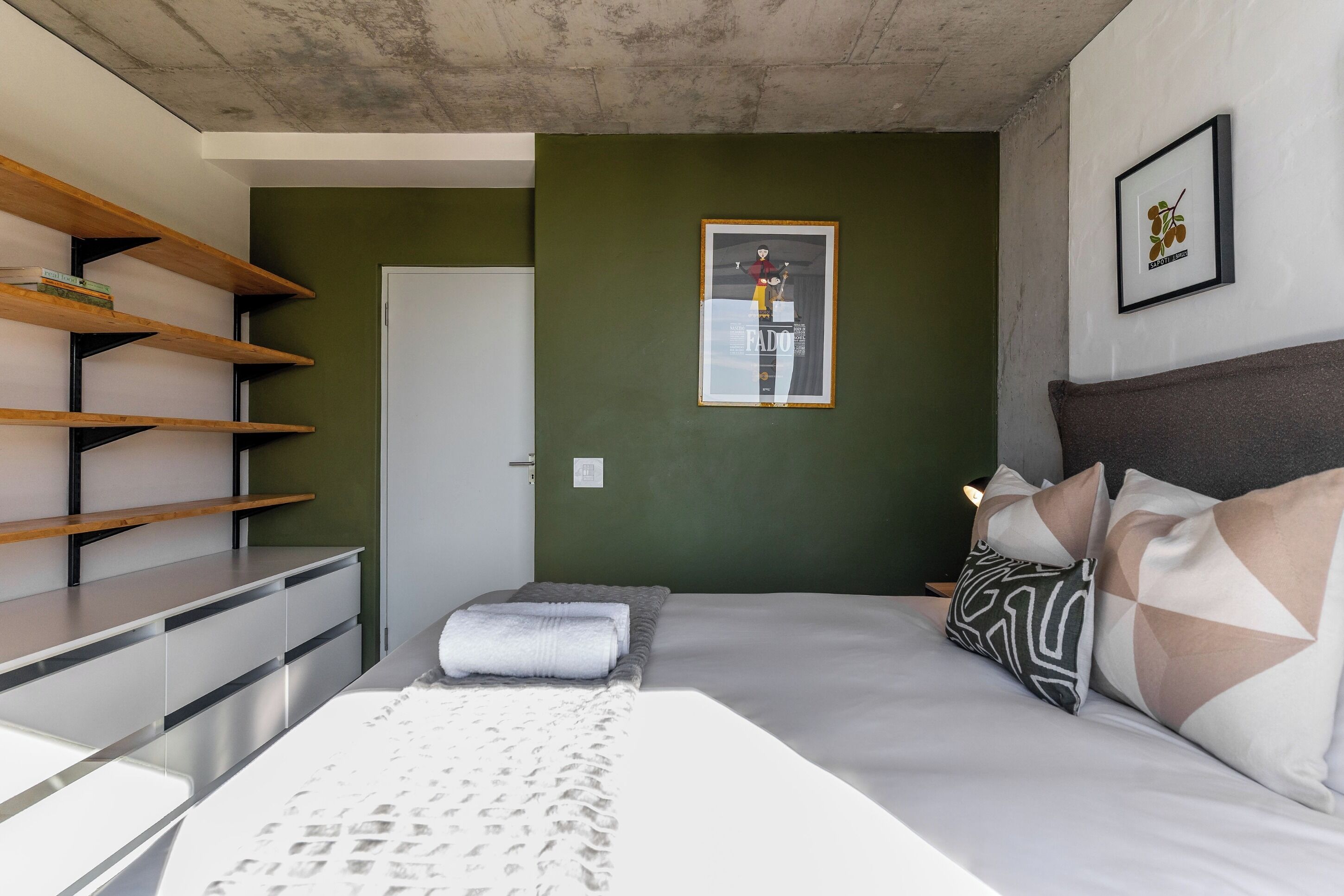 Un dormitorio moderno con una cama, almohadas, un taburete pequeño y una estantería.