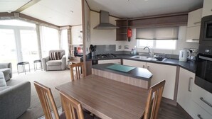 Een compacte keuken met een centraal kookeiland, een eethoek met een houten tafel en stoelen, en een kitchenette met een magnetron en fornuis.