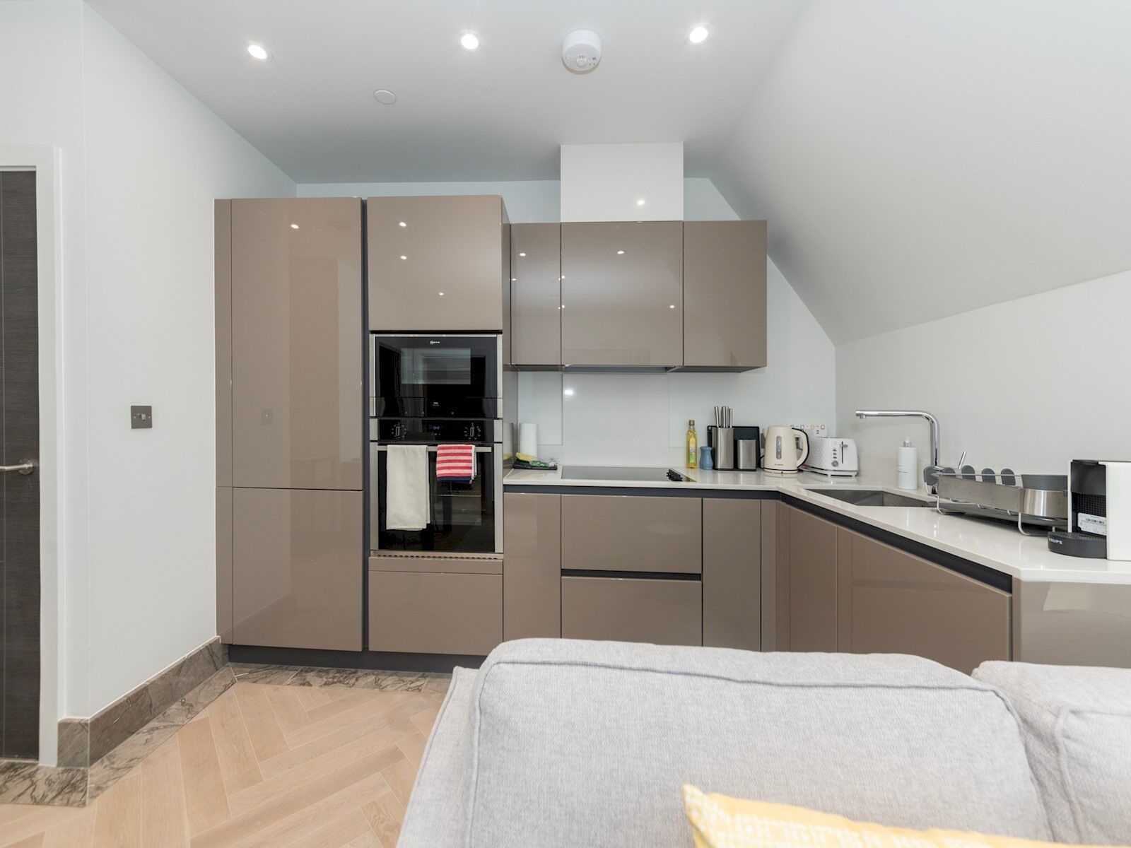 A modern kitchen with built-in appliances, a countertop with a kettle, and a sink.