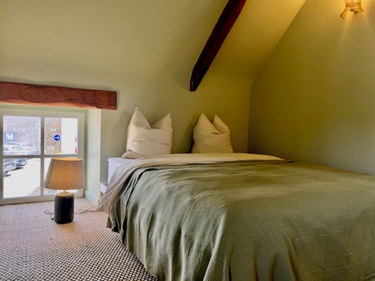 A bedroom with a bed, pillows, a lamp, and a view through a window.