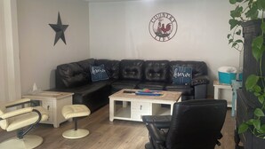 A living room with a black leather sofa, two white armchairs, a coffee table, and a black chair. A wall decoration with a rooster and the words "Country Life" is visible. - Spacious Century 3-bed in Downtown Wellington with in Ground Pool and parking! (Prince Edward)