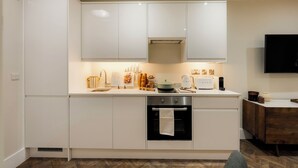 Una cucina moderna con mobili bianchi, forno integrato, macchina del caffè e una TV a schermo piatto montata a parete.