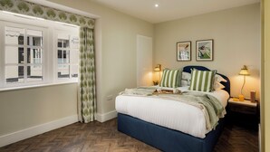 A bedroom with a large bed, two bedside lamps, a window with curtains, and a wall-mounted picture. - Clifton Road Apartments | No.1 (Bristol)