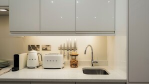 A modern kitchen with white cabinets, a stainless steel sink, a toaster, a coffee maker, and a jar of utensils. - Clifton Road Apartments | No.1 (Bristol)