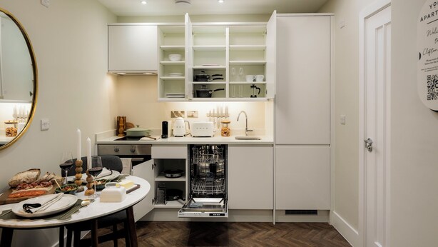 A compact kitchen with white cabinets, a dishwasher, and a dining area with a table set for a meal. - Clifton Road Apartments | No.1 (Bristol)