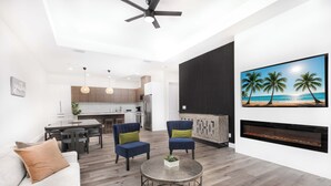 A modern living room with a sofa, two chairs, a coffee table, a fireplace, and a kitchen in the background.