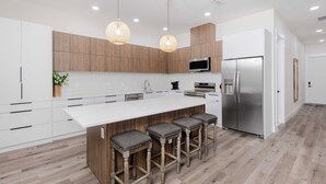 A modern kitchen with a large island, wooden cabinets, stainless steel appliances, and pendant lighting.