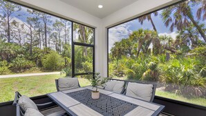 A dining area with a table and chairs, large windows with a view of a tropical landscape.