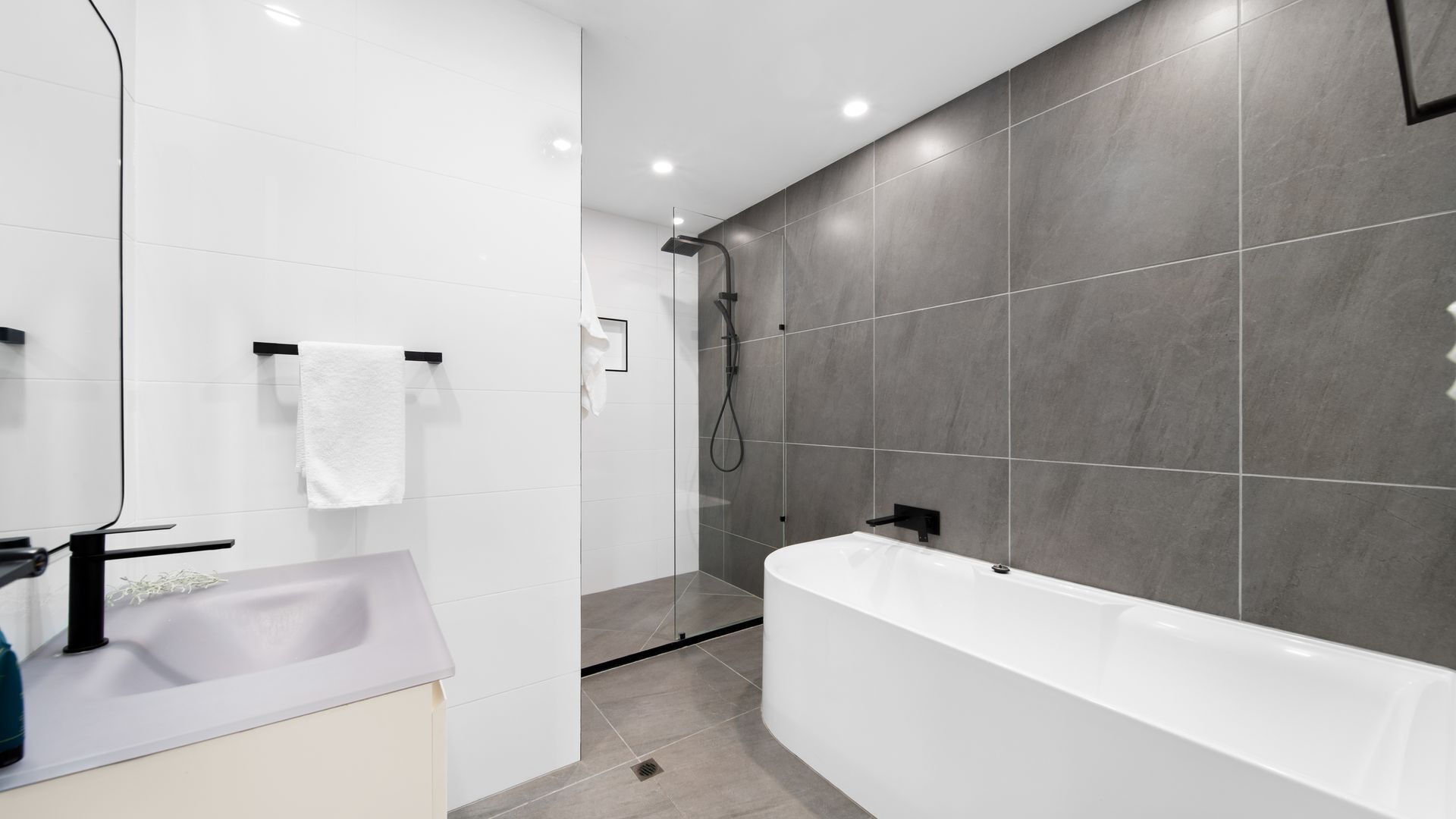 A modern bathroom with a white bathtub, a glass-enclosed shower, and a sink with a towel rack.