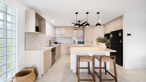 A modern kitchen with wooden cabinets, a central island, bar stools, and pendant lighting. - Unit 4 Tuscany Shores (Marcoola)
