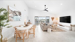 A modern living room with a dining area, a sofa, a TV, and a view of the outside. - Unit 4 Tuscany Shores (Marcoola)