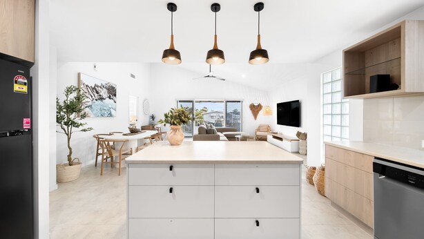 A modern kitchen with a central island, pendant lights, and a dining area with a view. - Unit 4 Tuscany Shores (Marcoola)
