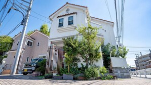 A two-story building with a white facade and a red-tiled roof. There is a car parked in front and a pedestrian bridge in the background. - Japanese-style family house in the western of Tokyo, DP Oyamamachi　 (町田市小山町)