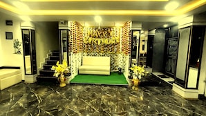 Un interior moderno con un sofá central, una escalera y una pared decorada con globos de 'HAPPY BIRTHDAY'.
