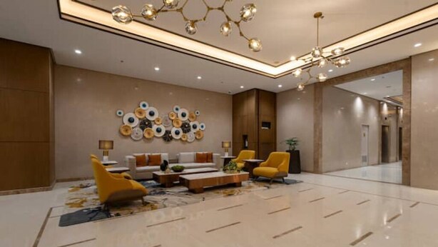 A spacious lobby with a modern chandelier, a seating area with yellow chairs, and a decorative wall art piece.
