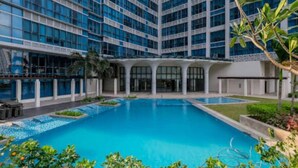 A modern hotel with a large central pool surrounded by greenery and a multi-story building with a grid of windows. - Luxury 1BR at BGC Uptown with Free Parking (Taguig City)