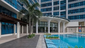 A modern hotel with a large indoor swimming pool, surrounded by palm trees and a covered walkway. - New & Modern Uptown BGC 1BR 4pax (Taguig City)