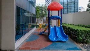 A playground with a slide and climbing structures, located in a modern urban setting with tall buildings nearby. - New & Modern Uptown BGC 1BR 4pax (Taguig City)