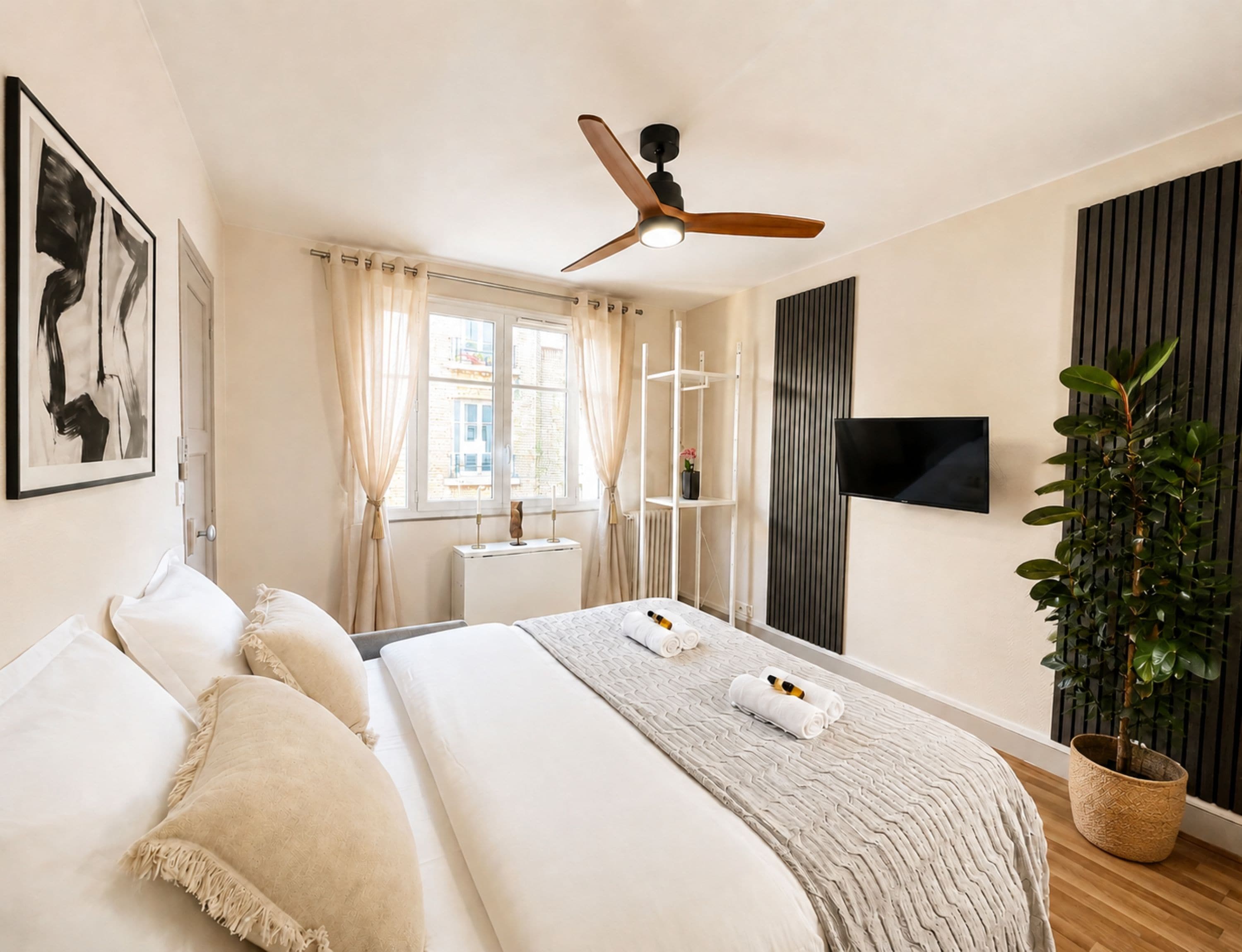 Ein Hotelzimmer mit einem Bett, einem Deckenventilator, einem Fernseher, einem Fenster mit Vorhängen und einer Topfpflanze.