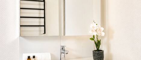 A modern bathroom with a white vanity, a large mirror, and a potted orchid.