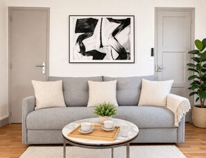Un soggiorno con un divano grigio, un tavolino da caffè con un vassoio e un quadro astratto in bianco e nero appeso alla parete.