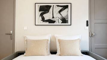 Habitación de hotel con una cama grande, dos almohadas, una obra de arte abstracta enmarcada, una puerta y toallas con botellas sobre la cama.