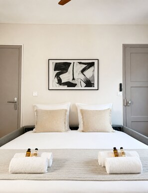 A hotel room with a large bed, two pillows, a framed abstract artwork, a door, and a towel with bottles on the bed. - 1566 Duranton (Paris)