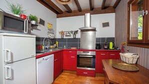 Une cuisine avec des meubles de rangement rouges, une hotte de cuisinière en acier inoxydable, un four à micro-ondes et un lave-vaisselle.
