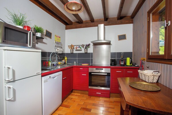 A kitchen with red cabinets, a stainless steel range hood, a microwave, and a dishwasher. - Au coeur des Soms en Chartreuse (Saint-Pierre-de-Chartreuse)