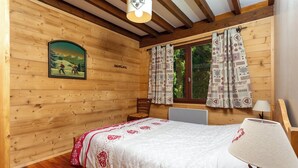Une pièce de cabane en bois comprenant un lit, une chaise, une table et une fenêtre avec des rideaux.
